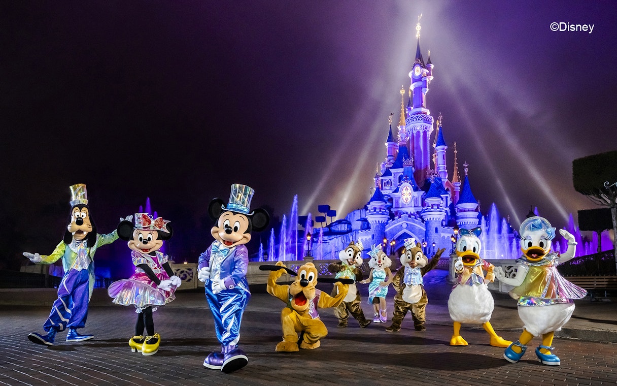 Disney characters in front of illuminated Sleeping Beauty Castle at Disneyland Paris.