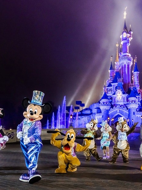 Disney characters in front of illuminated Sleeping Beauty Castle at Disneyland Paris.