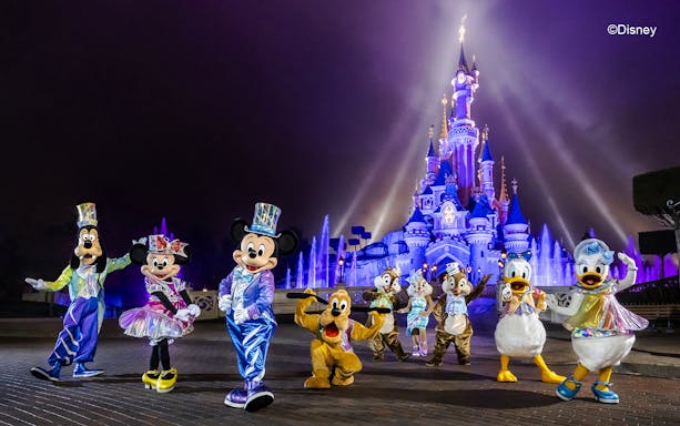 Disney characters in front of illuminated Sleeping Beauty Castle at Disneyland Paris.