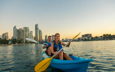 Kayakers paddling at sunset with Gold Coast skyline in the background.