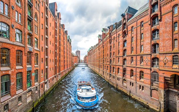 Boat cruising through Hamburg's Speicherstadt canal with historic brick warehouses.