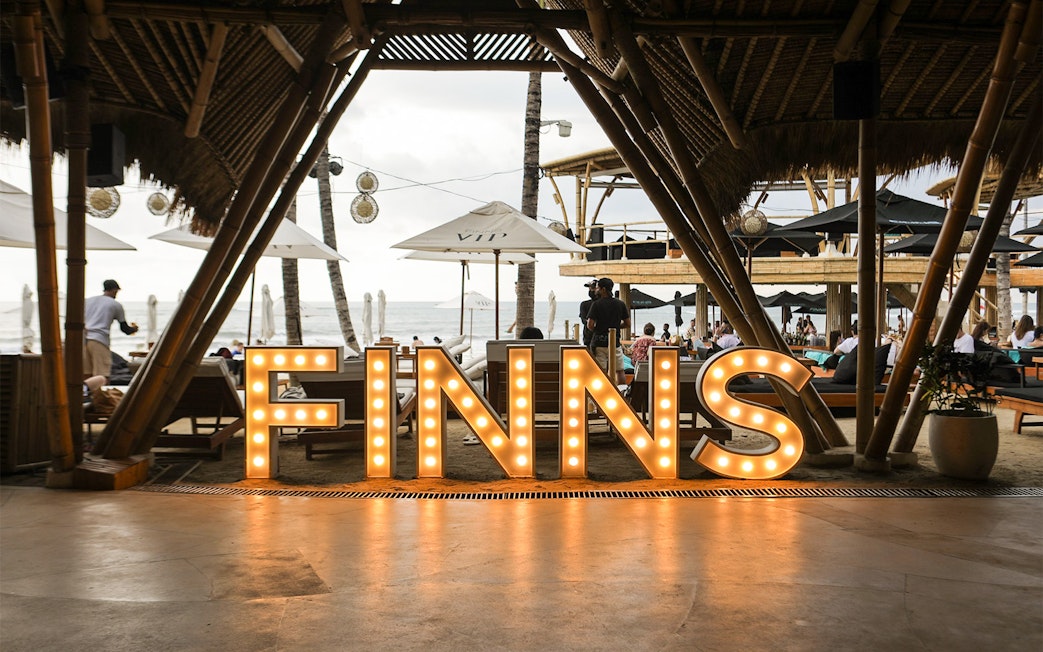Finns Beach Club entrance with illuminated sign, Bali beachfront view.