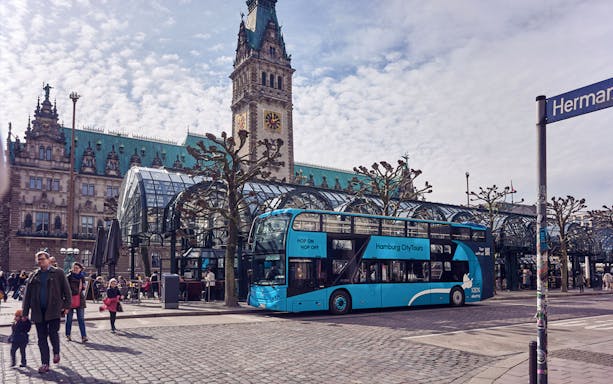Hamburg HopOn HopOff bus at Rathausmarkt stop with city hall in background.