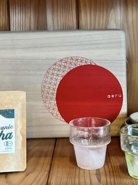 Organic matcha package with glass cups and ceramic bowls on a wooden shelf.