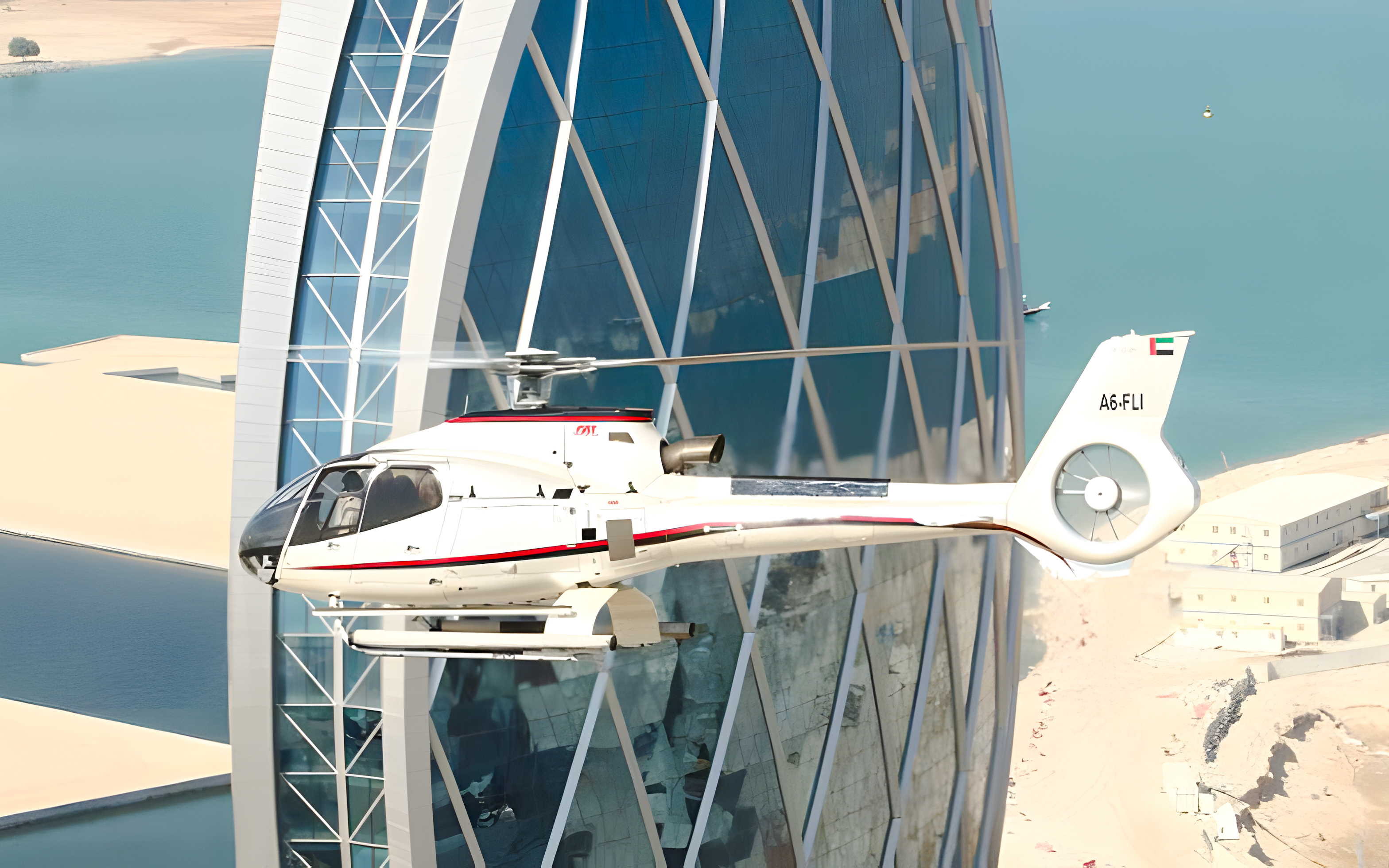 Helicopter flying near a modern skyscraper in Dubai with a view of the coastline.