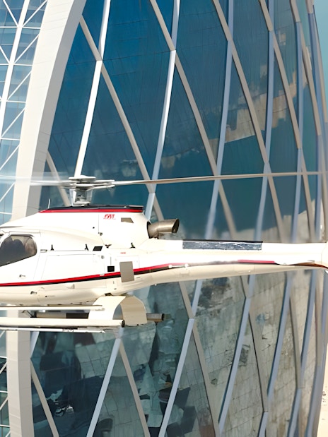 Helicopter flying near a modern skyscraper in Dubai with a view of the coastline.