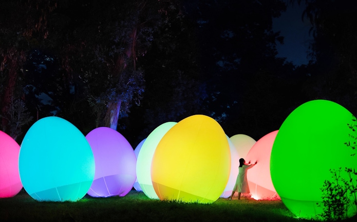 Visitors interacting with colorful digital art installations at teamLab Botanical Garden, Osaka.