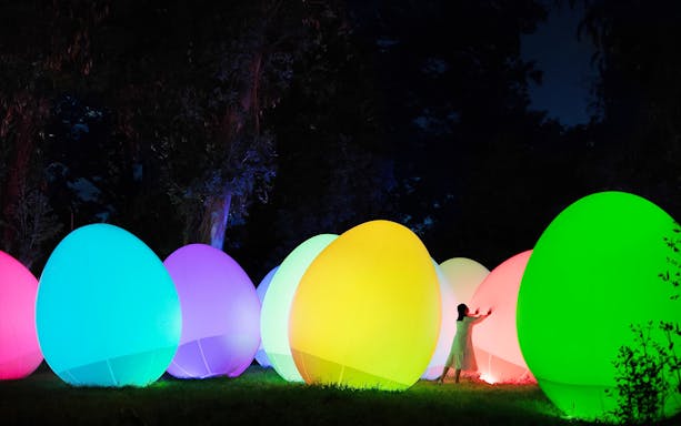 Visitors interacting with colorful digital art installations at teamLab Botanical Garden, Osaka.