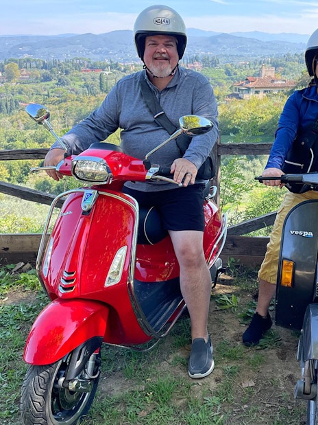 Two people on Vespas with a scenic view of Tuscany during a guided tour from Florence.