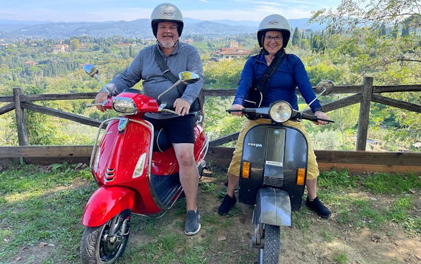 Two people on Vespas with a scenic view of Tuscany during a guided tour from Florence.