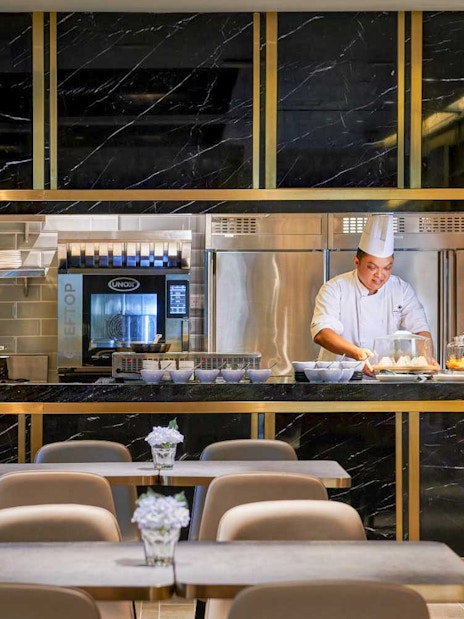 Chef preparing food at Plaza Premium Lounge kitchen counter.