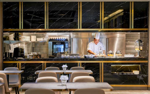 Chef preparing food at Plaza Premium Lounge kitchen counter.