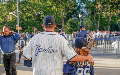 Father and daughter in Yankees jerseys outside stadium before New York Yankees vs Boston Red Sox game.