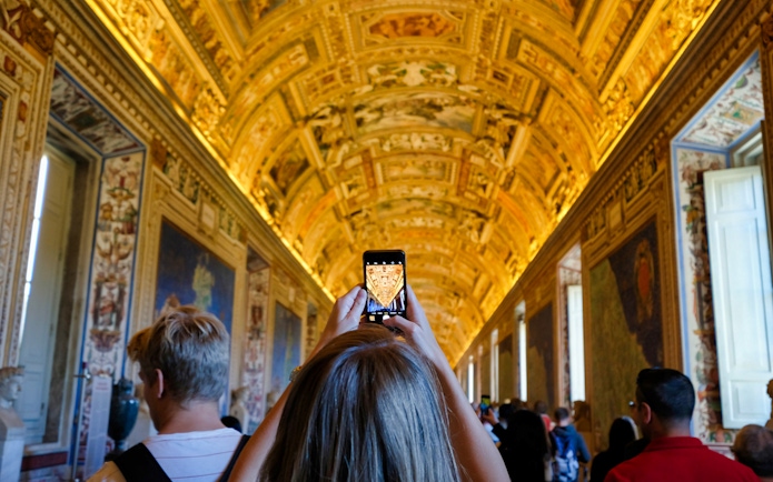 Tourists photographing ornate ceiling in Vatican Museum, Rome.