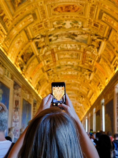 Tourists photographing ornate ceiling in Vatican Museum, Rome.