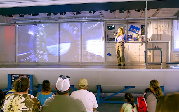 Staff presenting to guests at Houston Space Center with space shuttle model in background.
