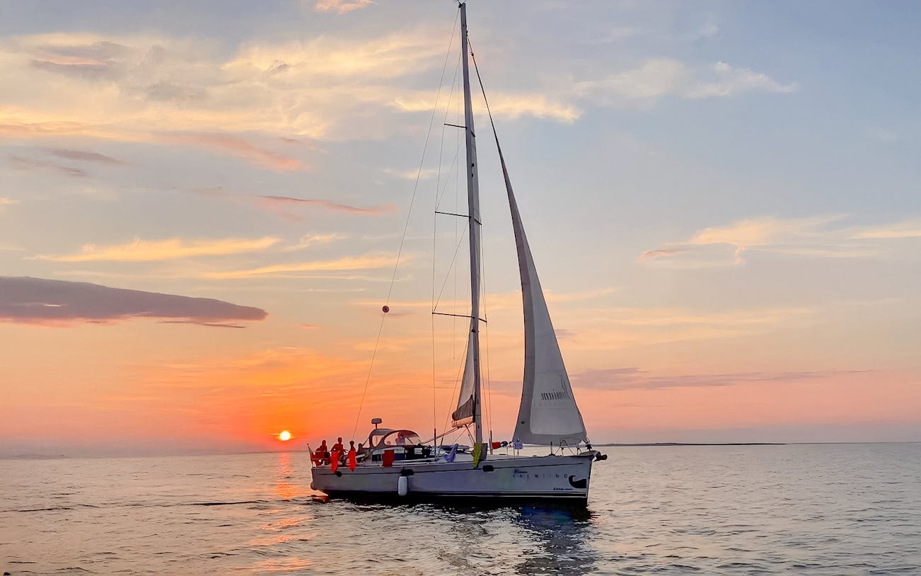 Sailboat on Gdansk River during sunset cruise with vibrant sky.