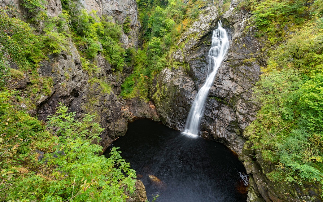 Waterfall cascading into a rocky pool surrounded by lush greenery in the Highlands near Loch Ness.