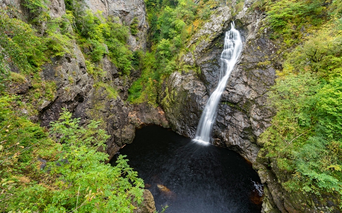 Waterfall cascading into a rocky pool surrounded by lush greenery in the Highlands near Loch Ness.