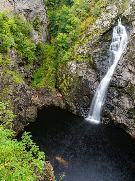 Waterfall cascading into a rocky pool surrounded by lush greenery in the Highlands near Loch Ness.
