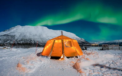 Tent under Northern Lights in snowy Tromsø landscape.