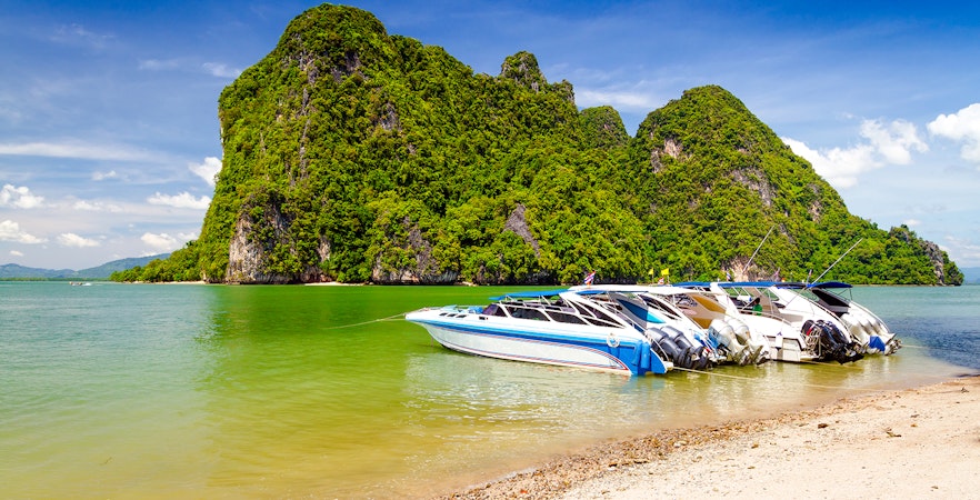 Motor boats docked on the coast of Phang Nga National Park, Thailand, with limestone cliffs in the background.