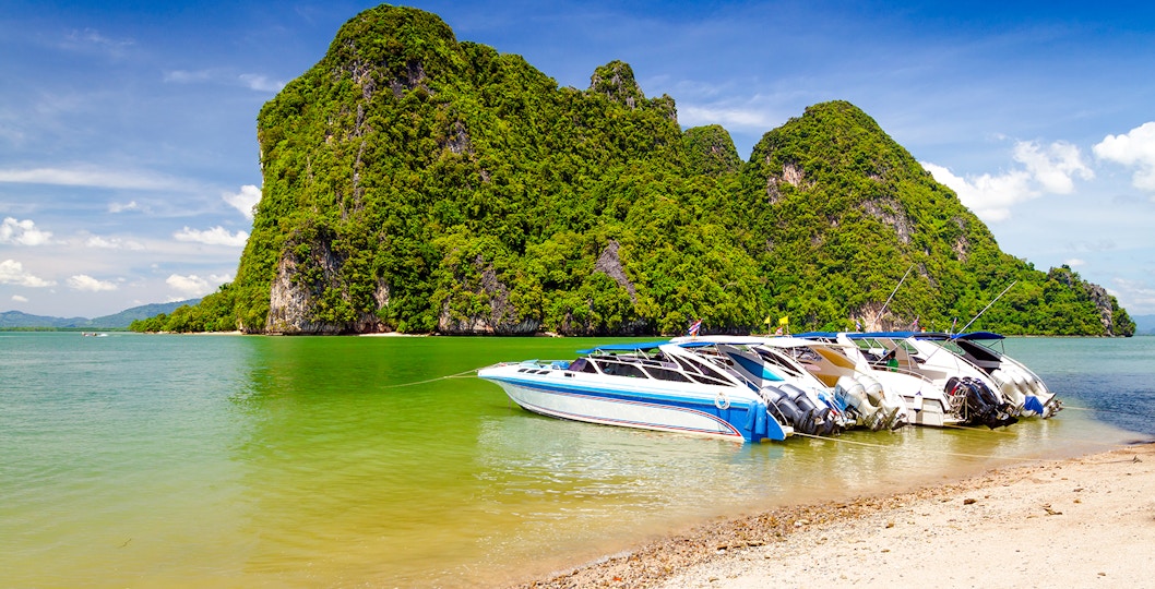 Motor boats docked on the coast of Phang Nga National Park, Thailand, with limestone cliffs in the background.