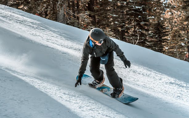 Snowboarder gliding down a snowy slope with forest backdrop, part of Ultimate Starter Skiing Pass.