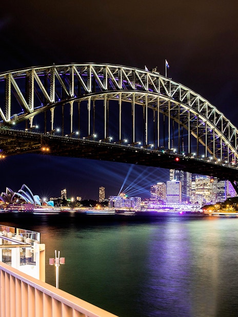 Sydney Harbour Bridge illuminated at night with city skyline and Opera House in view.