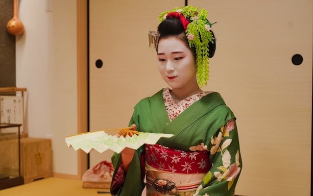 Geisha in traditional attire holding a fan during Gion Walking Tour in Kyoto.