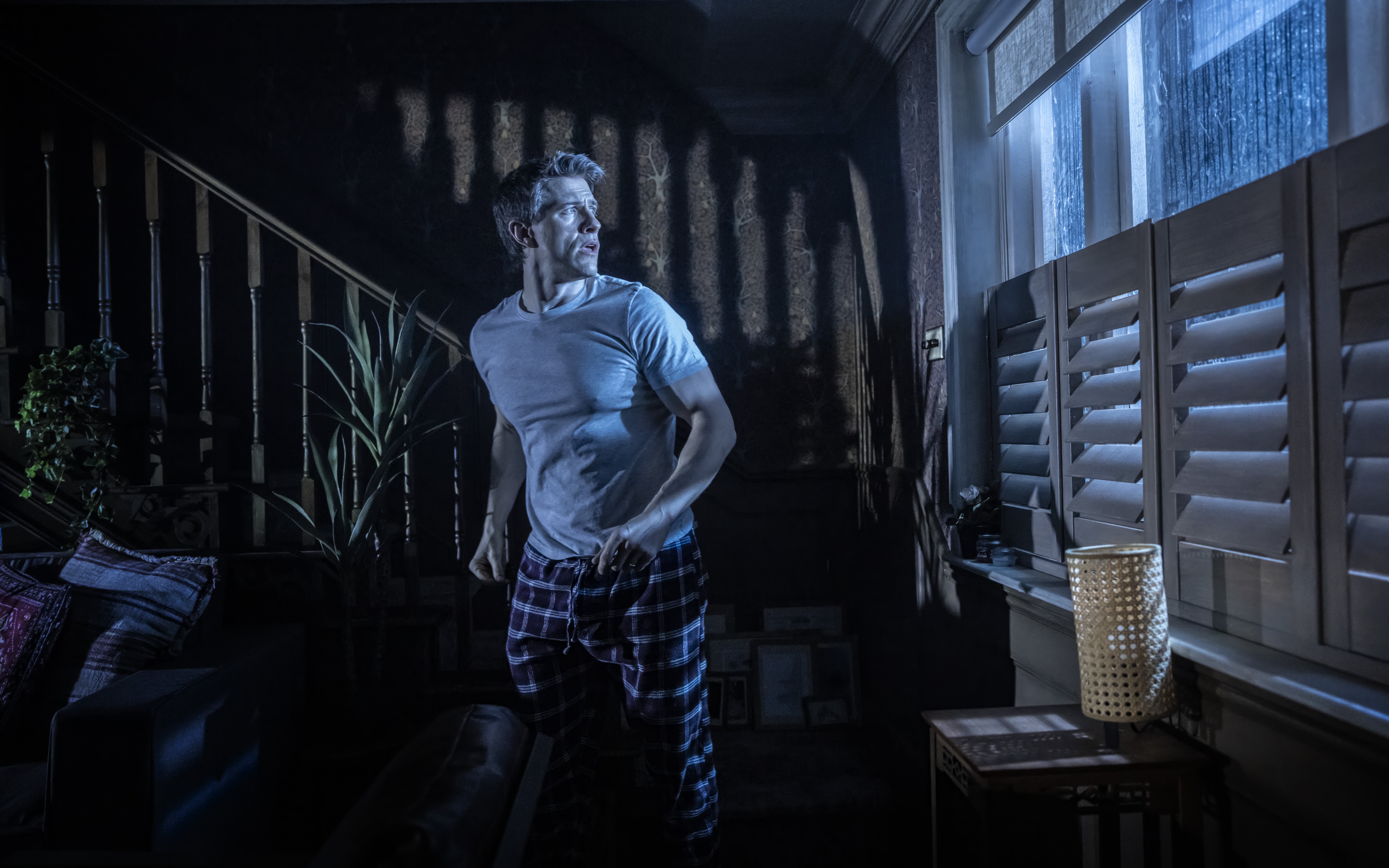 Man in a dimly lit room looking out a window during Paranormal Activity stage performance, Westend.