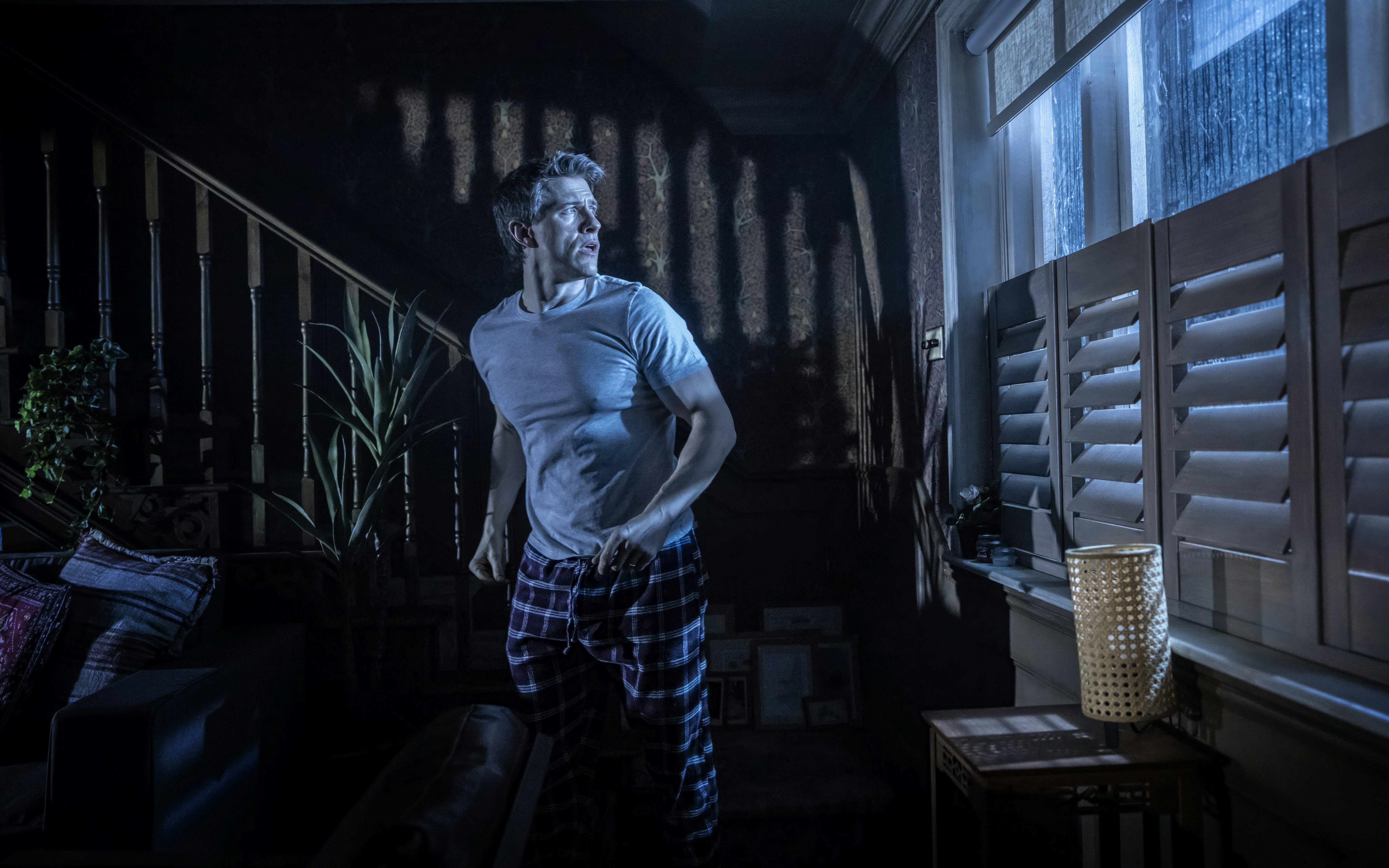 Man in a dimly lit room looking out a window during Paranormal Activity stage performance, Westend.
