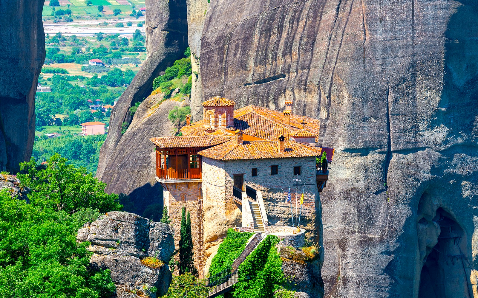 Holy Monastery of Roussanou perched on a rock formation in Meteora, Greece, surrounded by lush greenery.