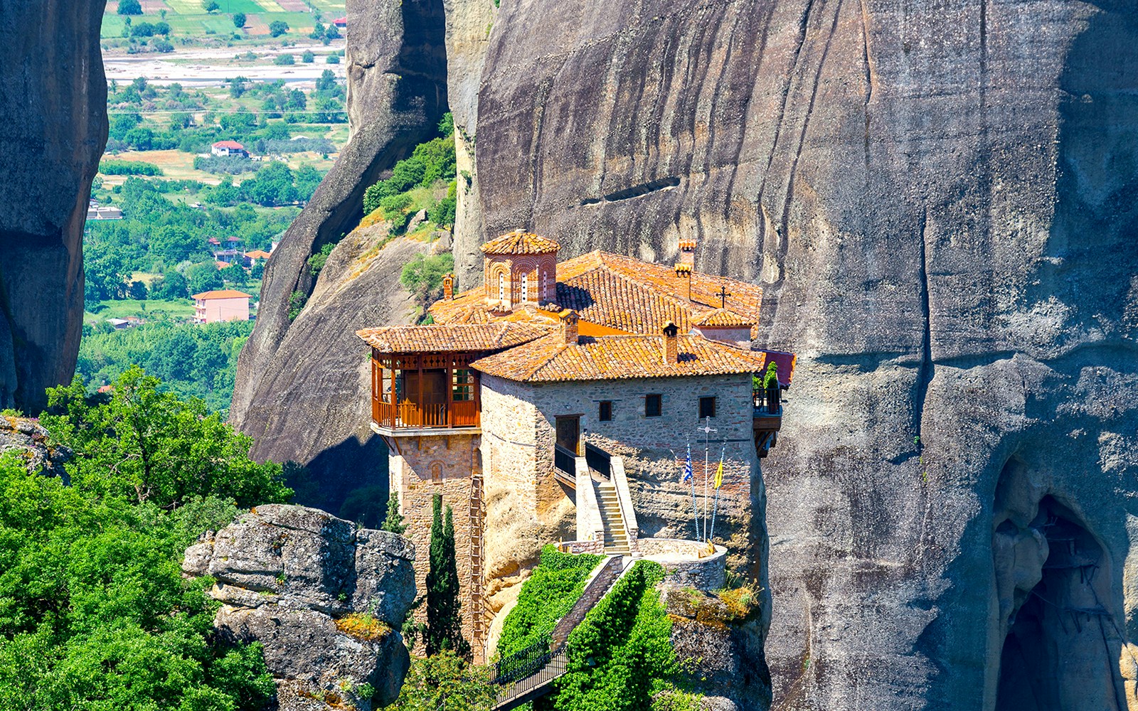 Holy Monastery of Roussanou perched on a rock formation in Meteora, Greece, surrounded by lush greenery.