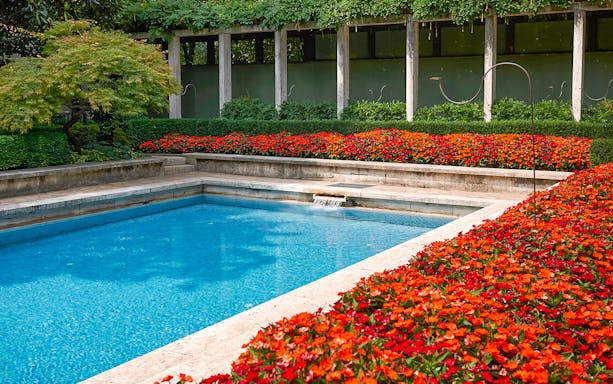 Villa Necchi Campiglio garden pool with vibrant red flowers and lush greenery.