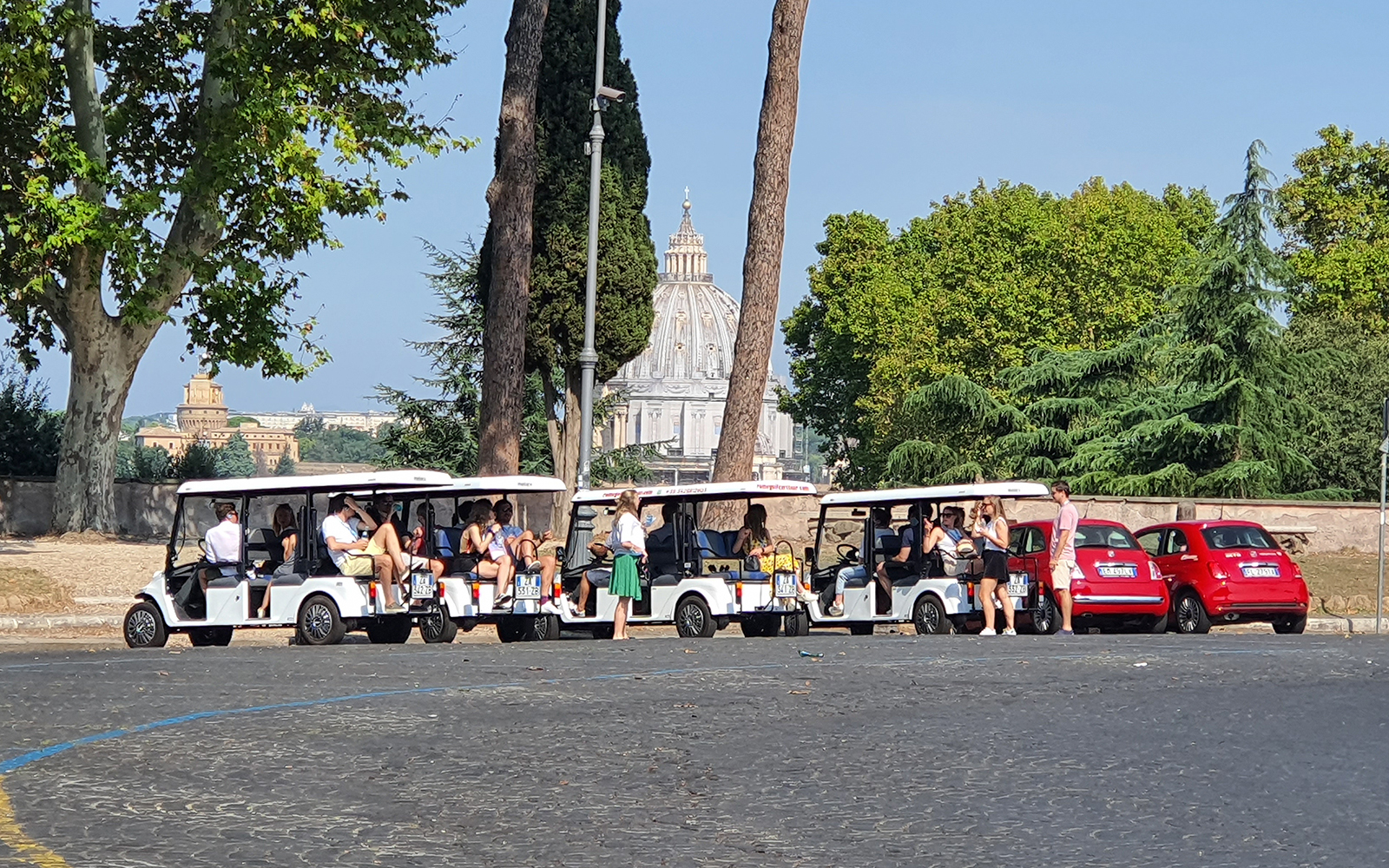 People touring Vatican City on golf carts with St. Peter's Basilica in the background.