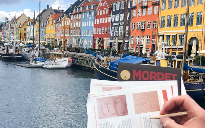 Nyhavn canal with colorful buildings and a person holding a mystery adventure booklet in Copenhagen.