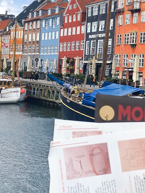 Nyhavn canal with colorful buildings and a person holding a mystery adventure booklet in Copenhagen.