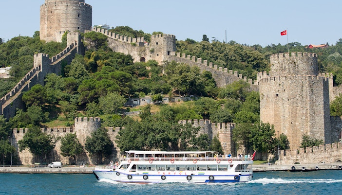 Bosphorus cruise boat with passengers, Istanbul skyline in background.