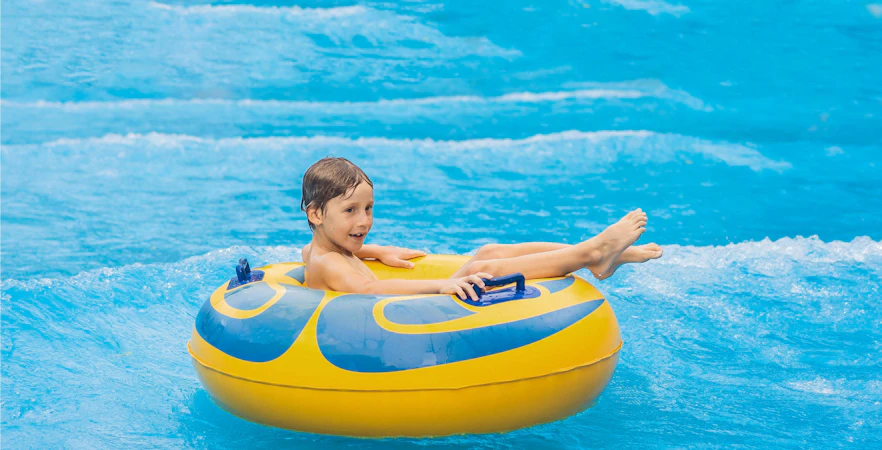 Boy on a yellow pool float in artificial waves at a water park.