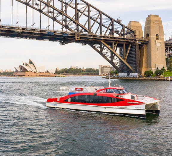 Sydney Harbour cruise boat passing under Harbour Bridge with Opera House in background.