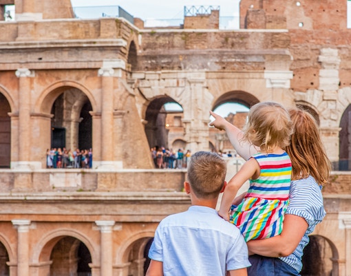Family exploring the Colosseum in Rome, child pointing at ancient arches.