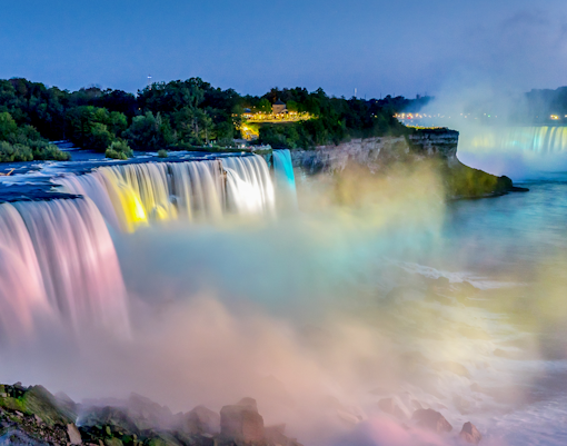 Niagara Falls illuminated at night with colorful lights and mist.