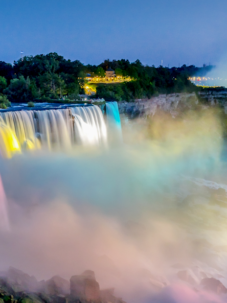 Niagara Falls illuminated at night with colorful lights and mist.