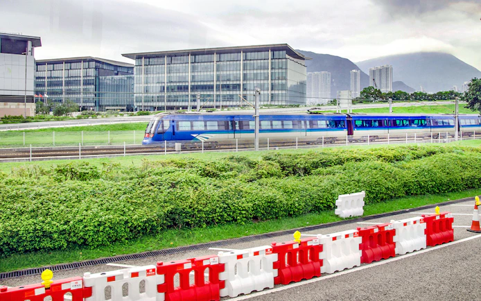 Train traveling between Hong Kong International Airport and city with modern buildings in background.