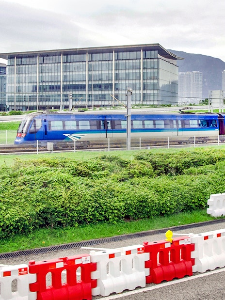 Train traveling between Hong Kong International Airport and city with modern buildings in background.