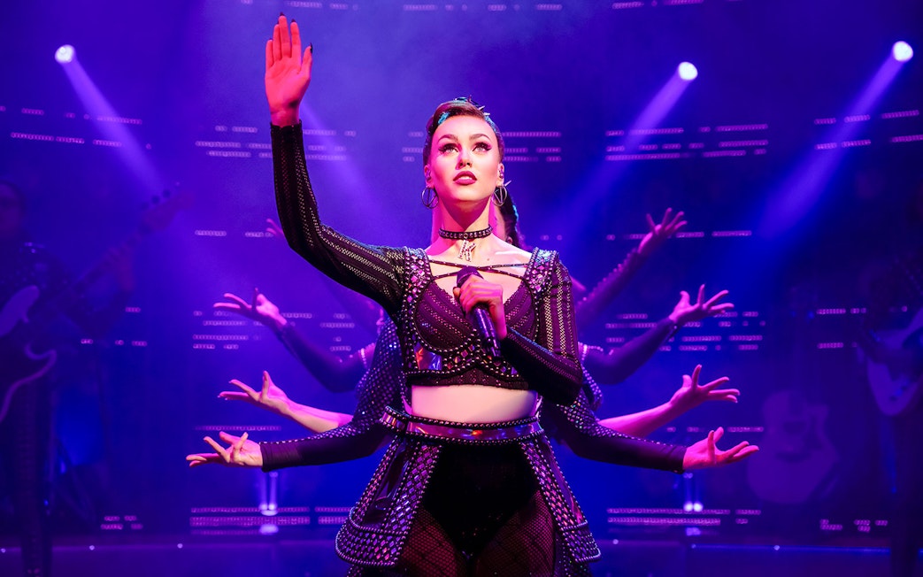 Performer on stage during "Six" musical with vibrant lighting.