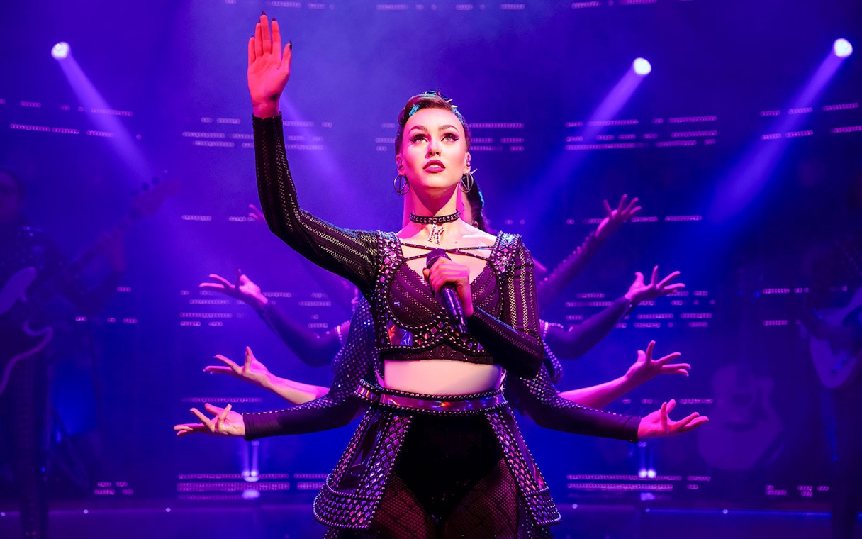 Performer on stage during "Six" musical with vibrant lighting.