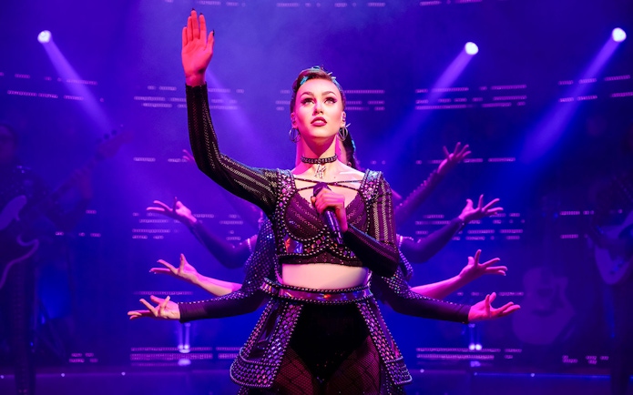 Performer on stage during "Six" musical with vibrant lighting.