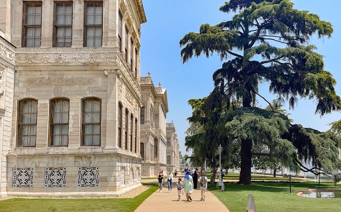 Walkway through Dolmabahçe Palace gardens with visitors and large tree, Istanbul.